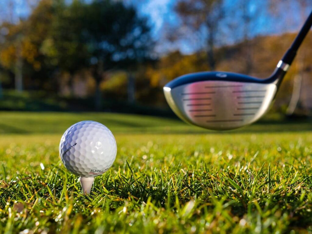 A golf ball and driver resting on green grass, representing the scenic golf courses in Queenstown.