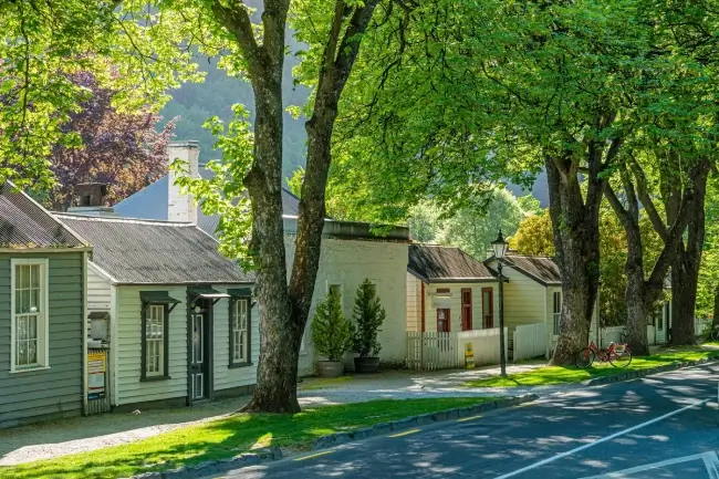 A picturesque street in Arrowtown featuring houses and trees, with the Arrowtown motel apartments in view.