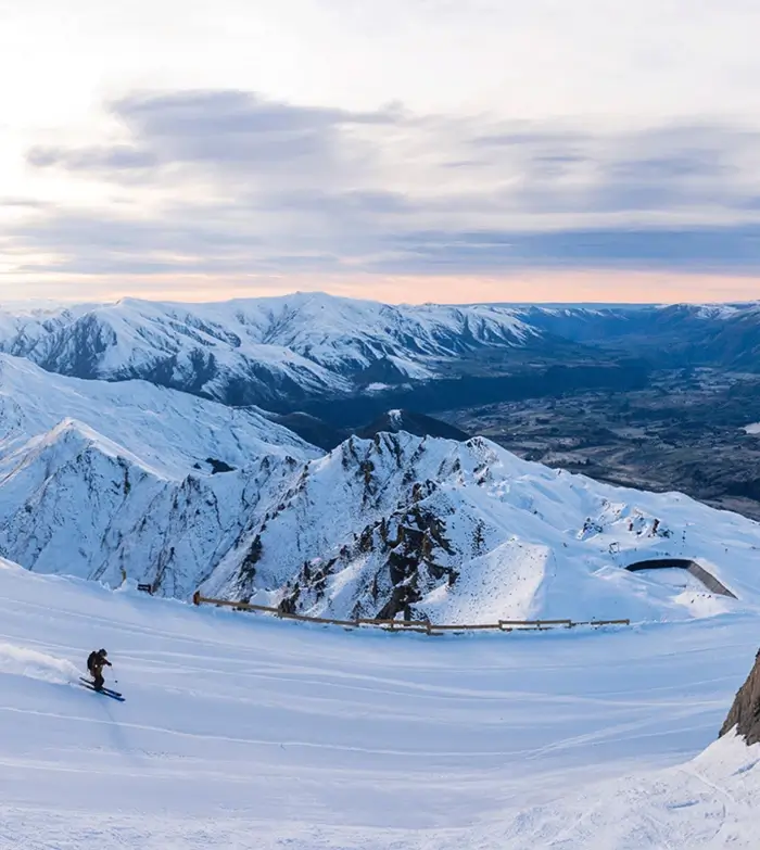 A person snowboards down a snowy mountain slope in Queenstown, showcasing winter sports excitement.